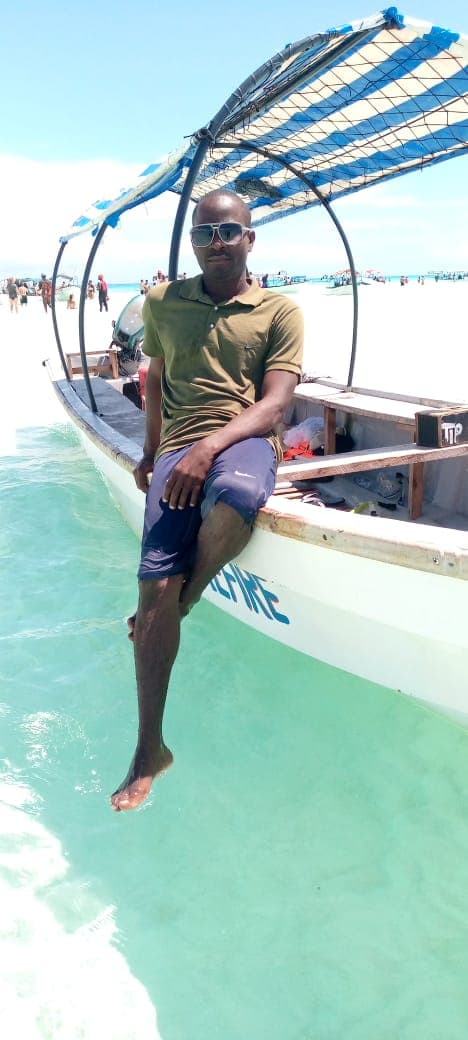 Haji, dein Local, auf einem traditionellen Dhow-Boot über türkisem Wasser vor Sansibar