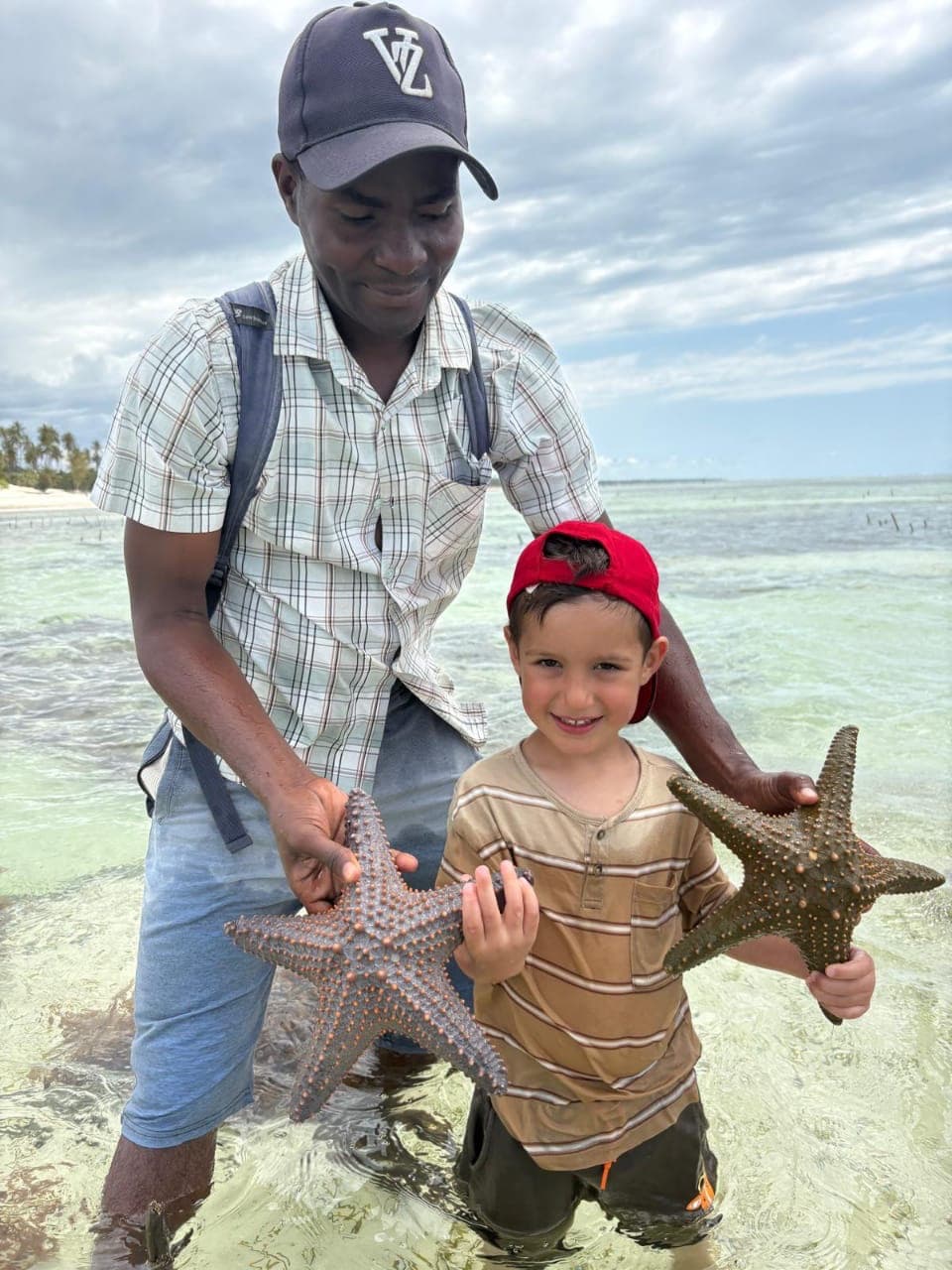 Lokalny mieszkaniec pokazuje dziecku rozgwiazdy w płytkiej wodzie na Zanzibarze