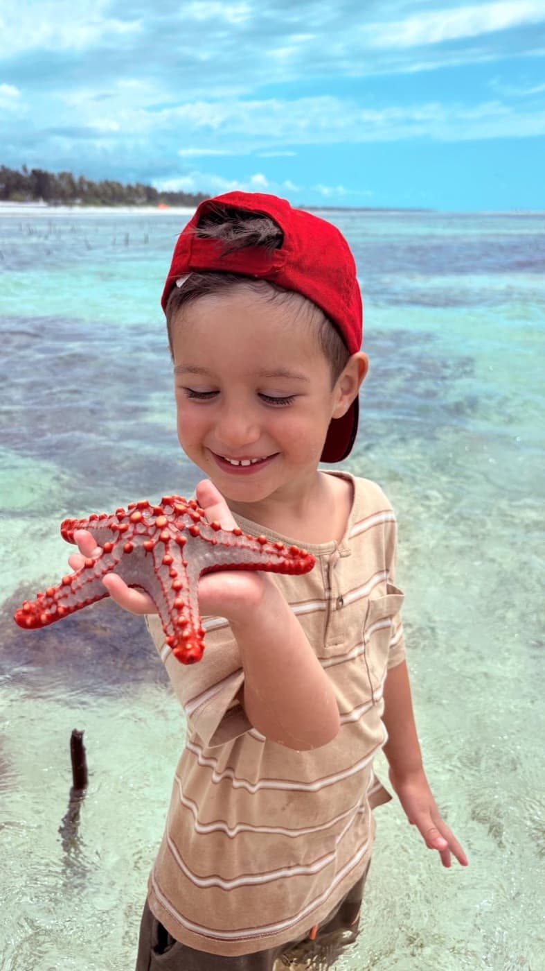 Un enfant tient fièrement une étoile de mer rouge dans l'eau peu profonde