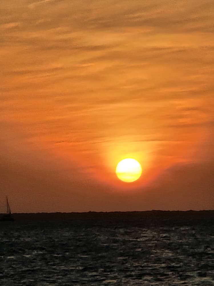 Glühend orangener Sonnenuntergang über dem Meer mit der Silhouette eines Dhows am Horizont vor Sansibar